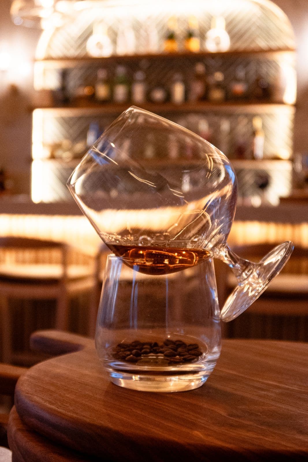 Ein Schwenkglas mit bernsteinfarbenem Getränk liegt schräg auf einem Glas voller Kaffeebohnen.