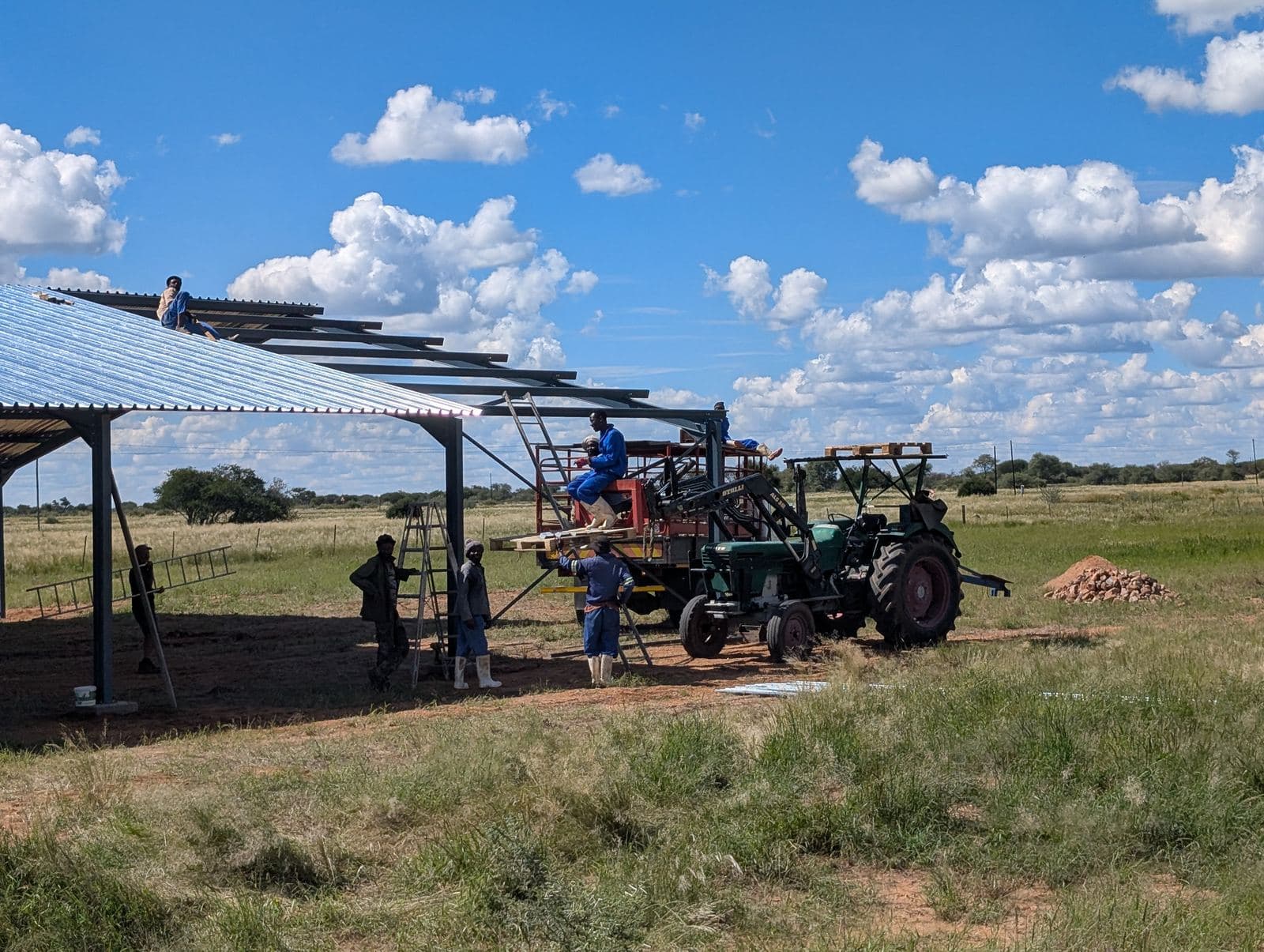 Auf der Farm entsteht eine neue Scheune: Stahlgerüst mit Wellblechdach, daneben ein Traktor.