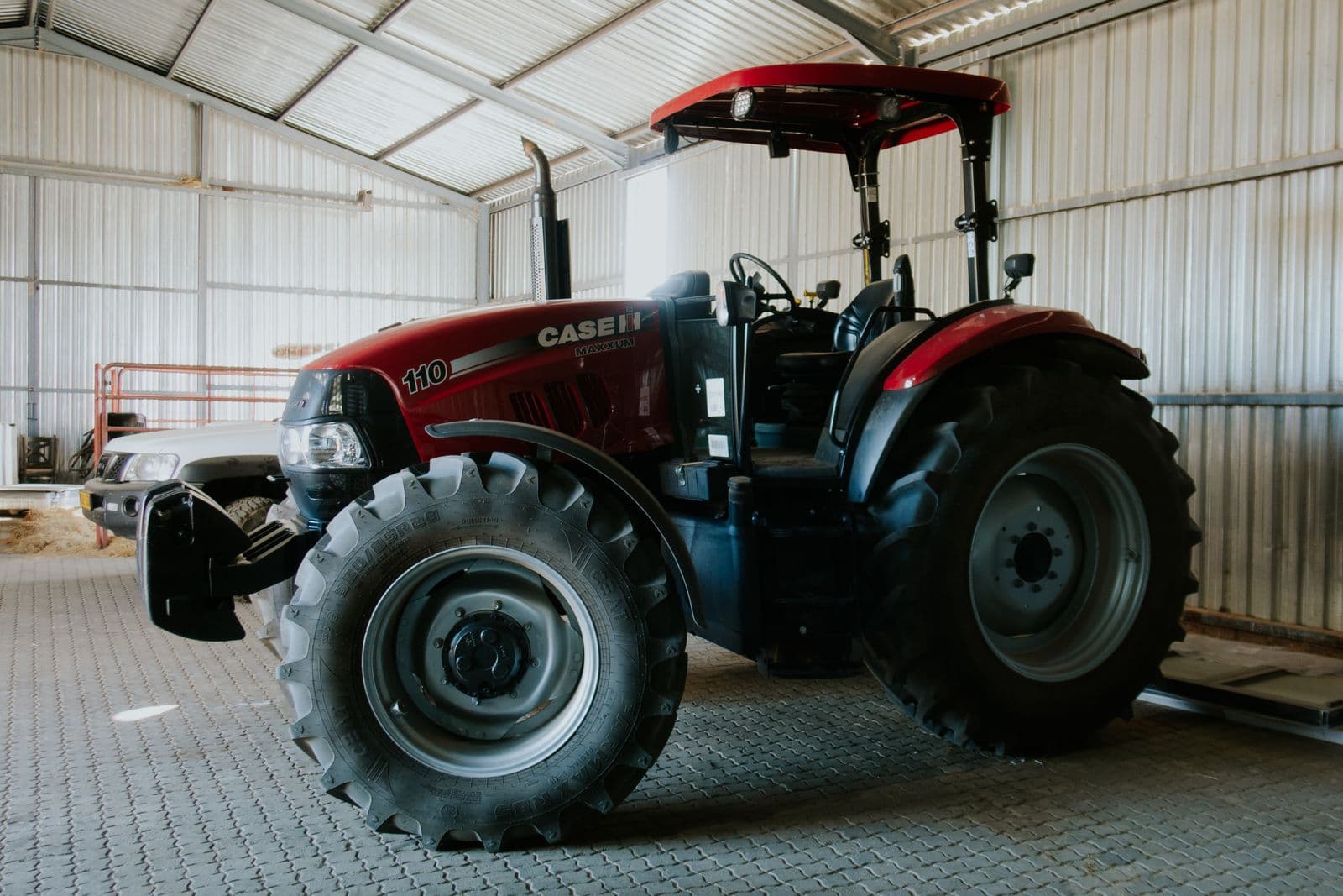 Ein roter Traktor in der offenen Halle, dahinter ein Pick-up.