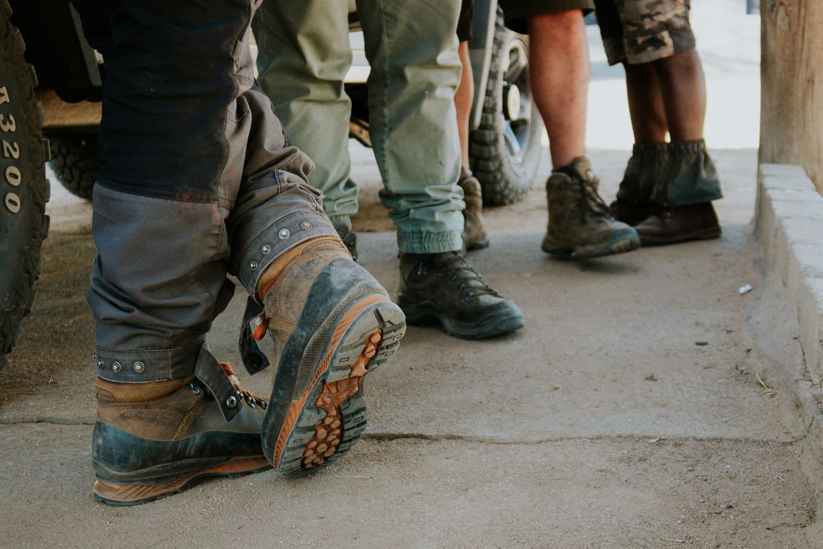 Wanderstiefel und Gamaschen von vier Personen, die vor dem Geländewagen stehen.