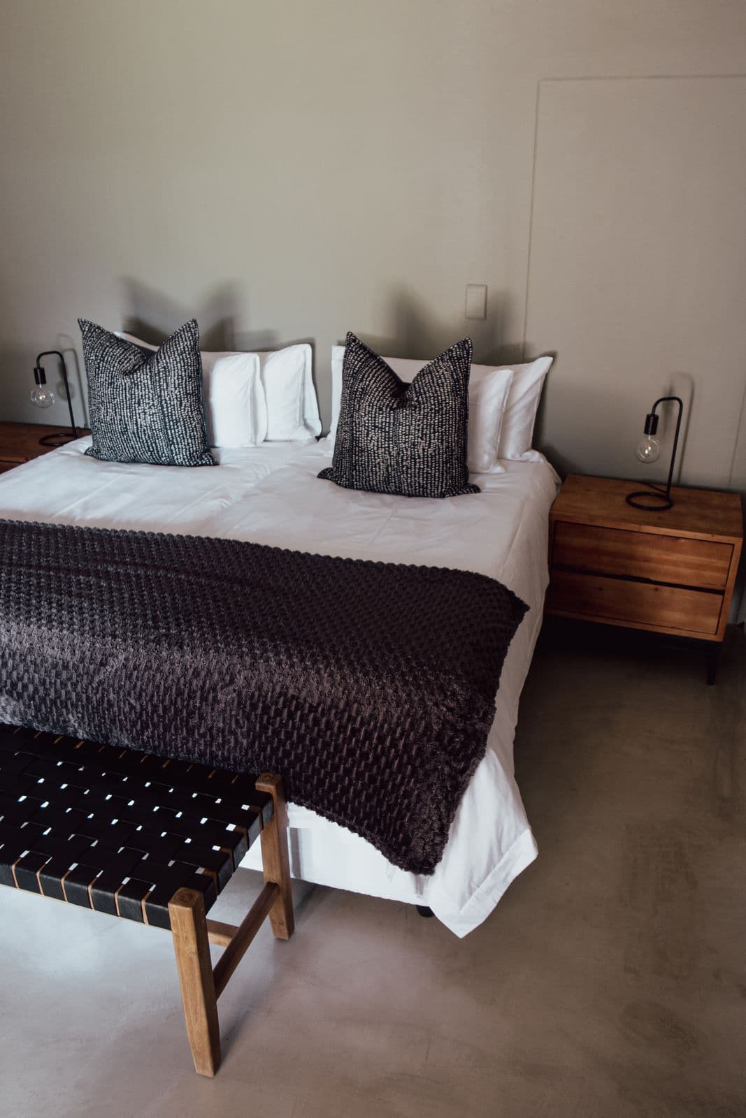 Schlafzimmer im Farmhaus: Doppelbett mit dunkler Decke, Nachttische mit Lampen auf beiden Seiten.