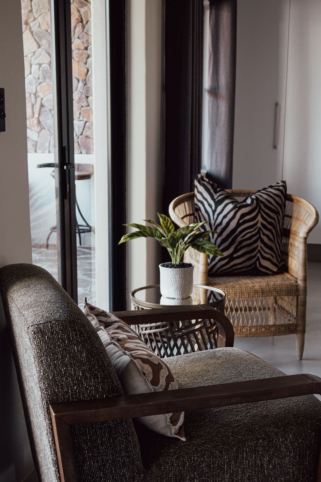 Sitzecke mit Rattansessel und Zebrakissen an der Glastür zur Terrasse.