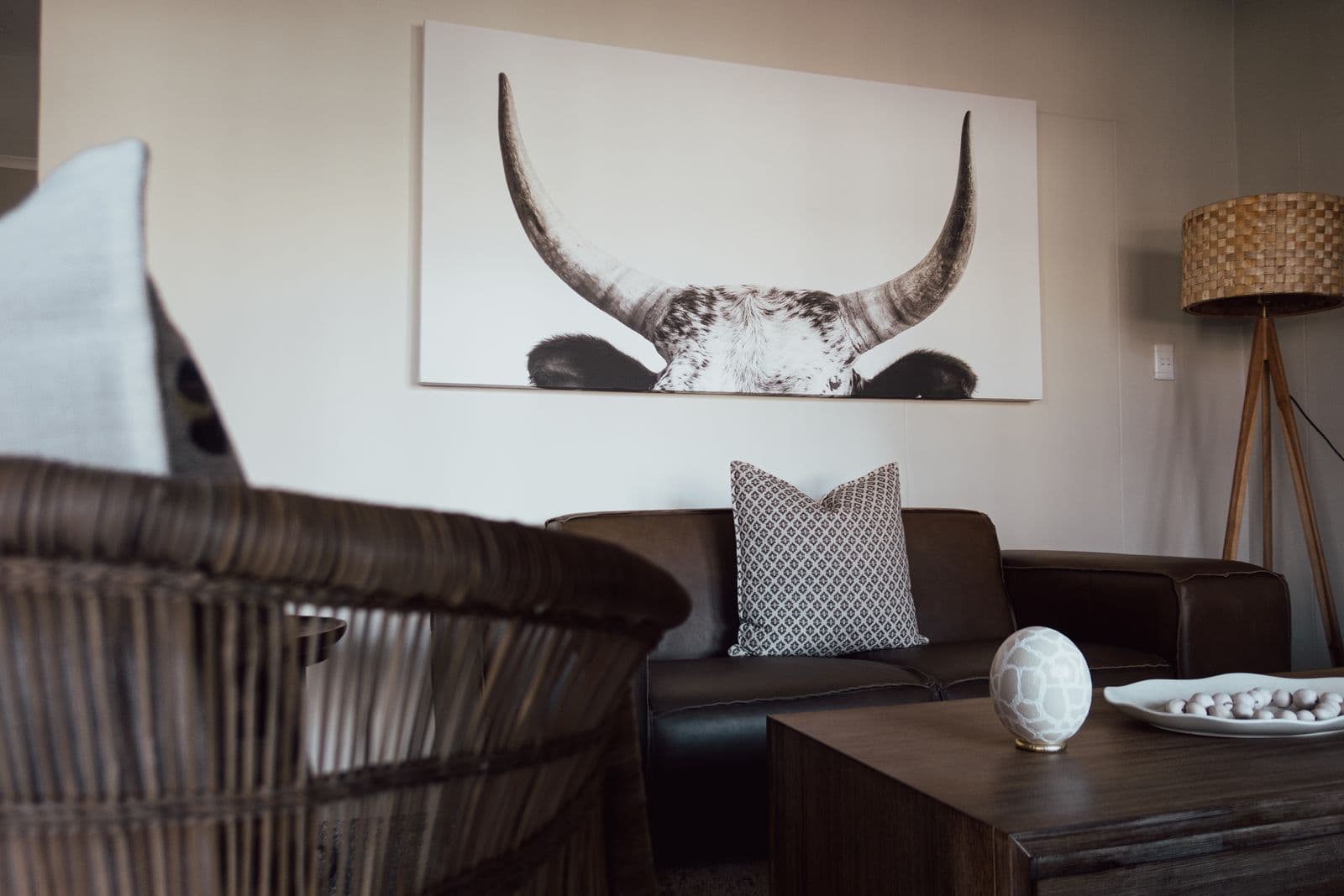 Der Wohnraum im Farmhaus mit Ledersofa, Rattansessel und dem großen Bild eines Longhorn-Rinds.
