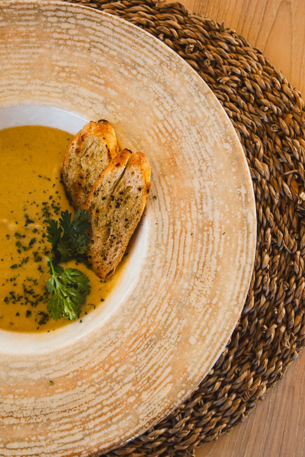 Gelbe Cremesuppe mit Kräutern und gerösteten Brotscheiben in einem tiefen Teller.