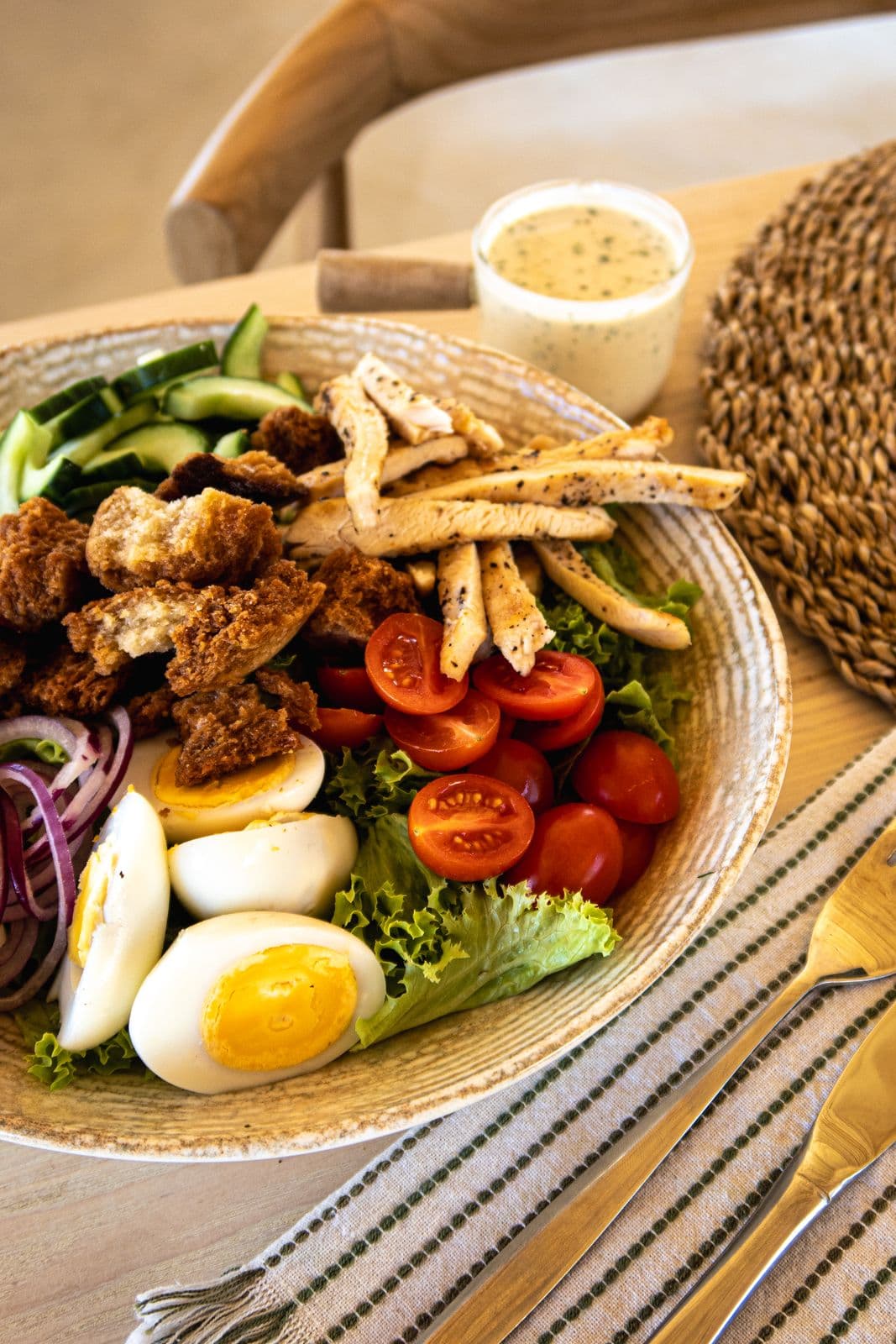 Bunter Salat mit Hähnchenstreifen, Croûtons, Kirschtomaten, Gurke und gekochten Eiern, dazu ein Dressing.