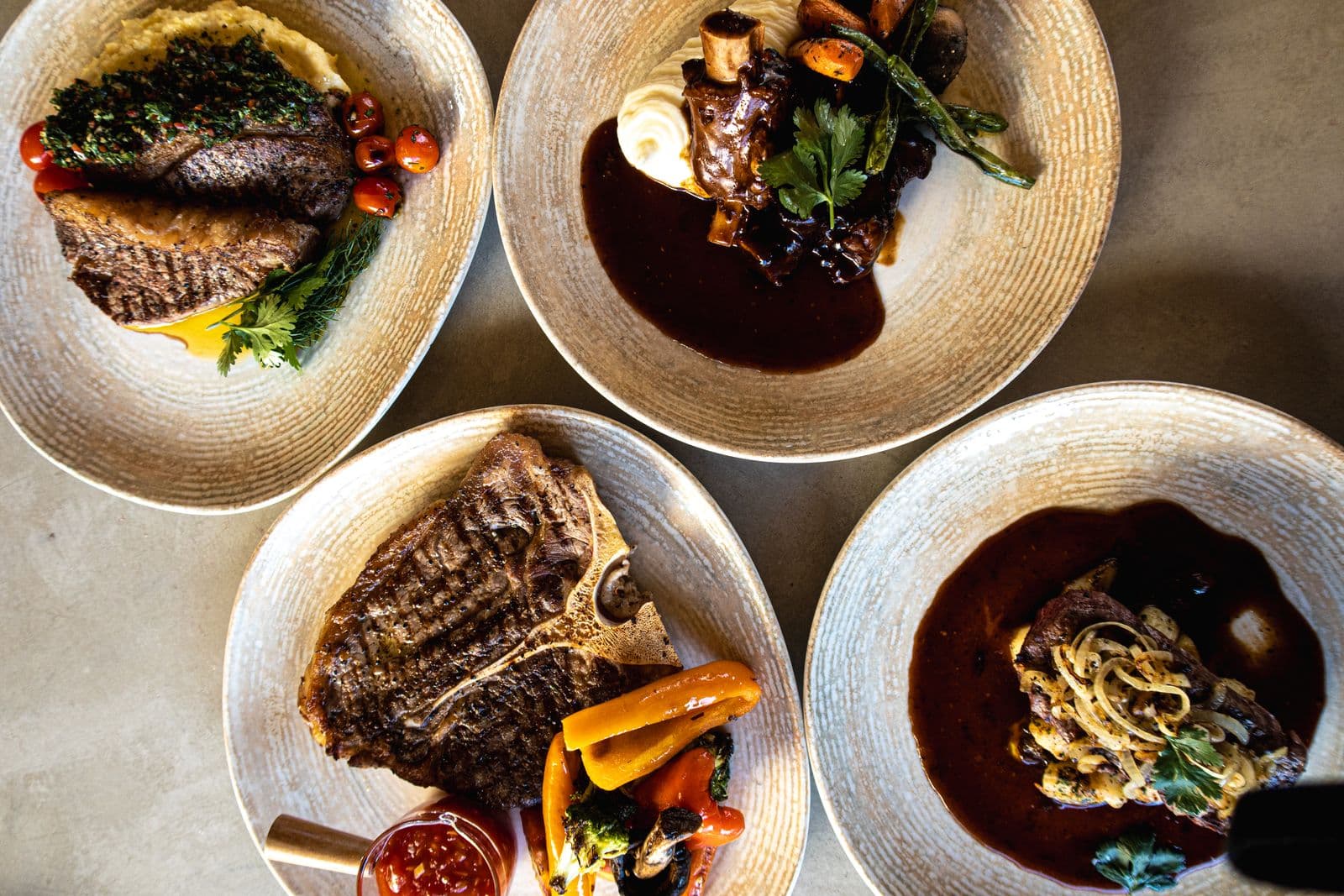 Vier Teller von oben: Steak mit Kräutersauce, Schmorfleisch, T-Bone-Steak mit Gemüse und Filet mit Röstzwiebeln in dunkler Sauce.
