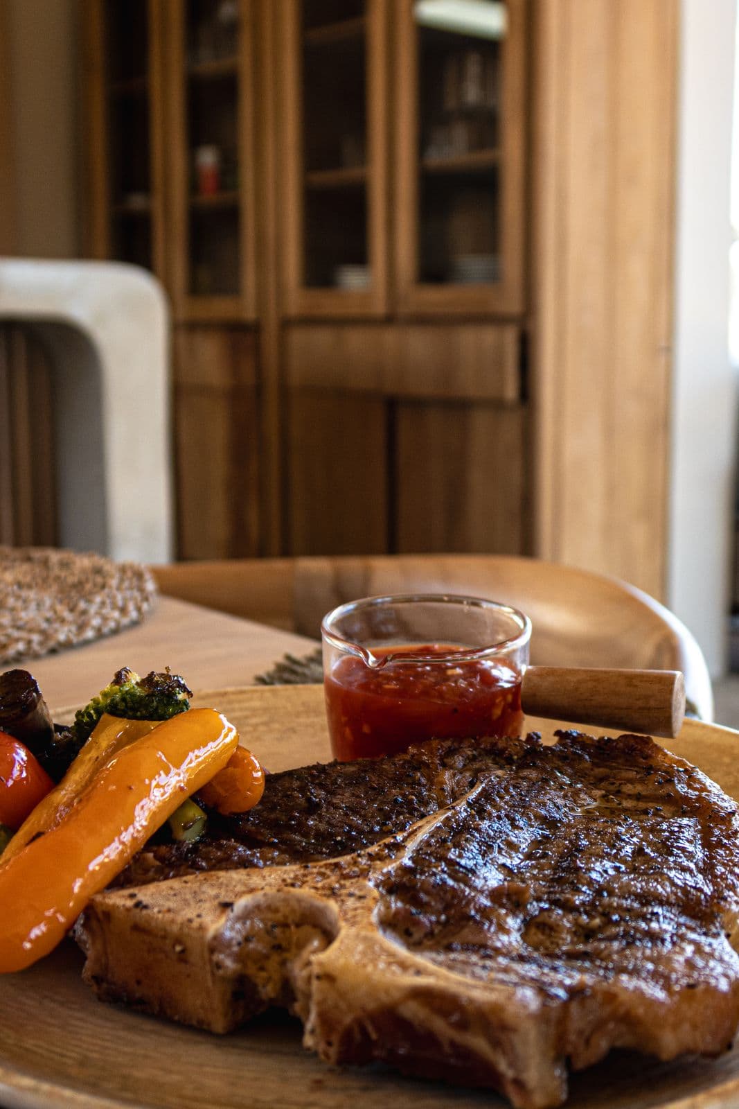 T-Bone-Steak vom Grill mit gebratenem Gemüse, dahinter ein Glas Tomatensalsa.