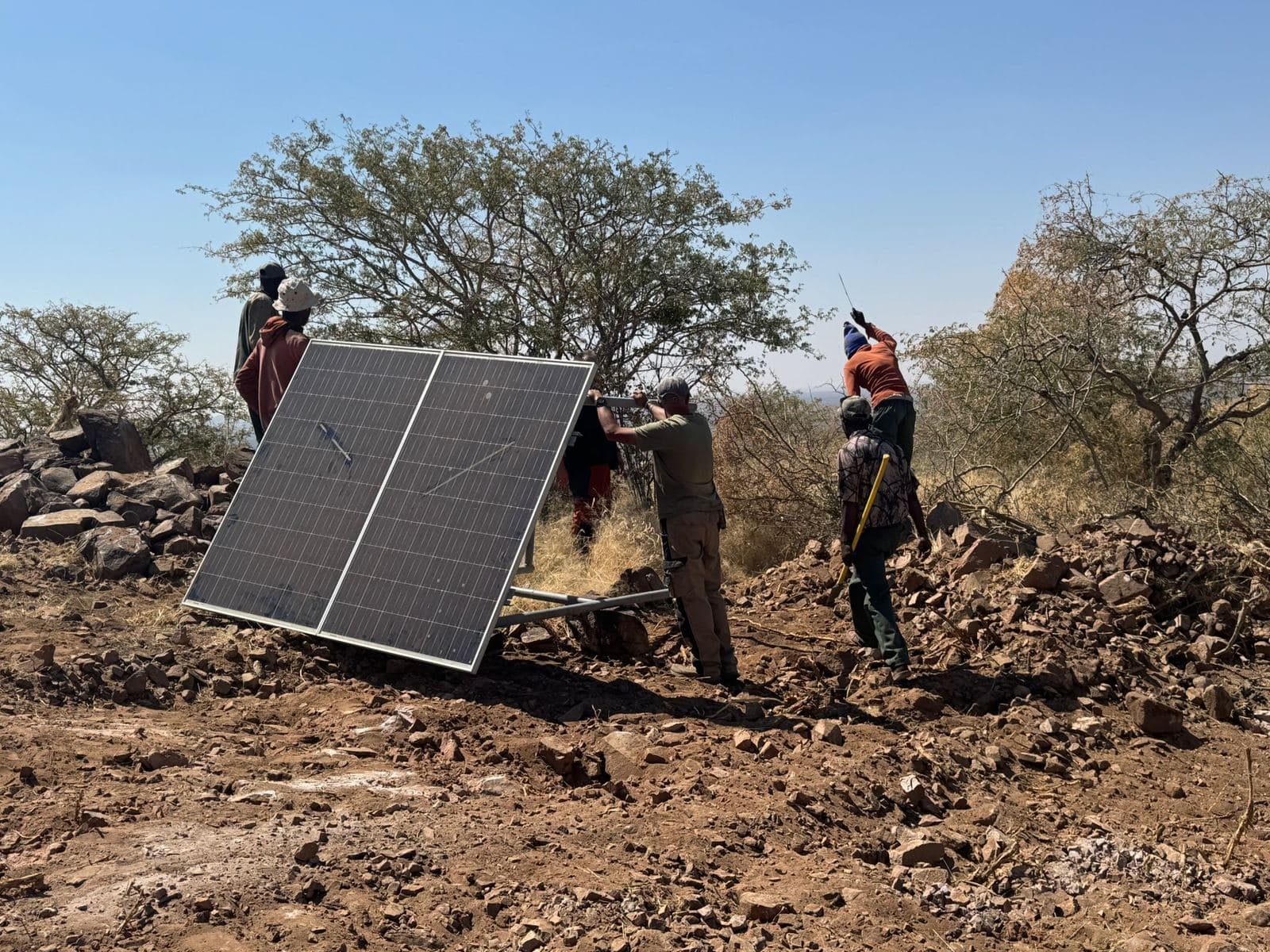 Mehrere Mitarbeiter richten auf felsigem Gelände ein Solarmodul auf.