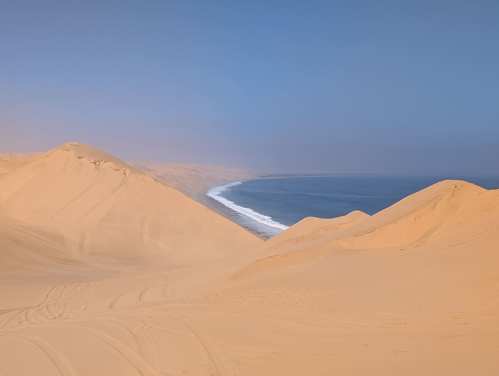 Hohe Sanddünen fallen zum Atlantik ab, an ihrem Fuß zieht sich die Brandung die Küste entlang.