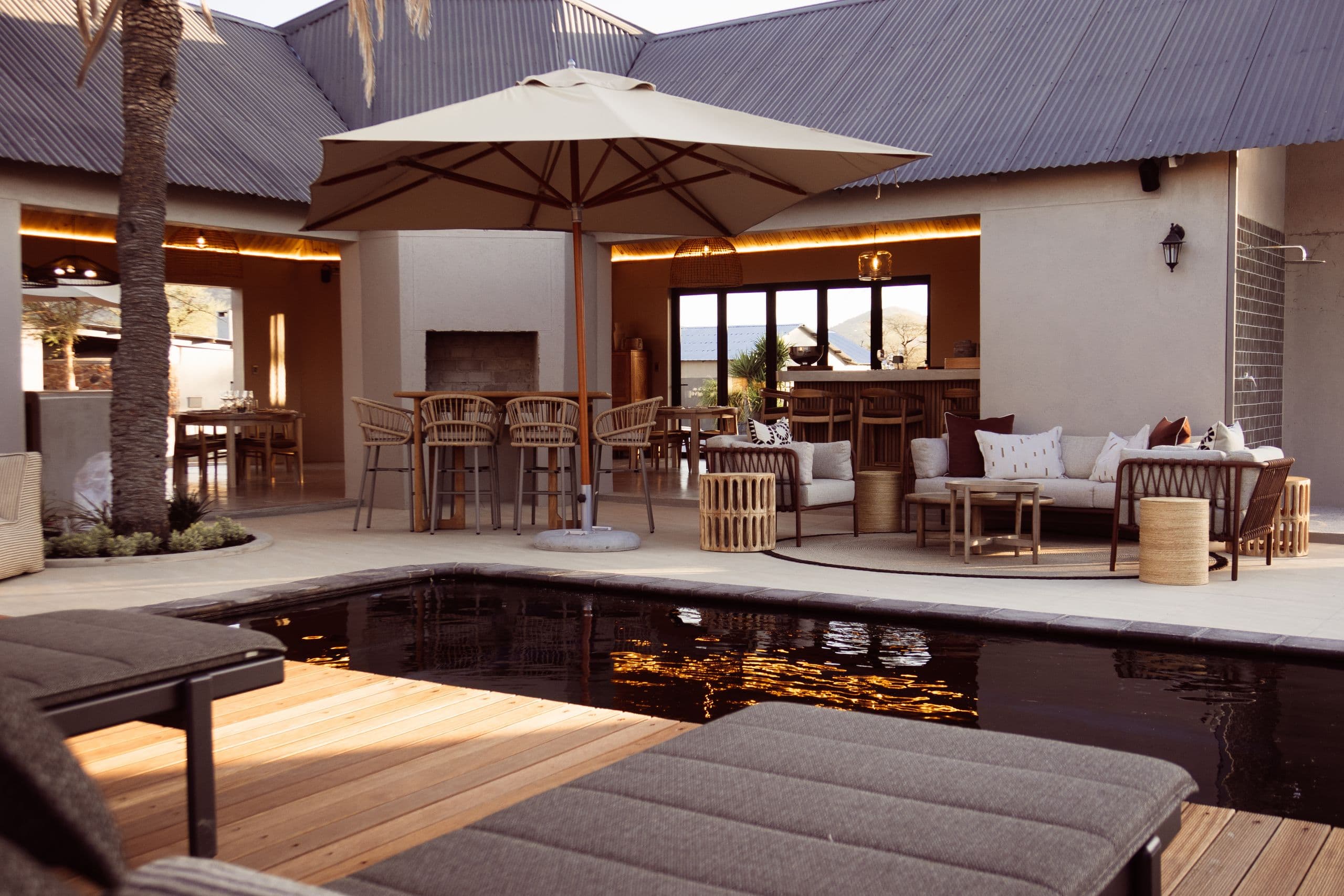 Der Pool am Abend, dahinter die offene Lapa mit Kamin, Bar und Lounge unter einem großen Sonnenschirm.