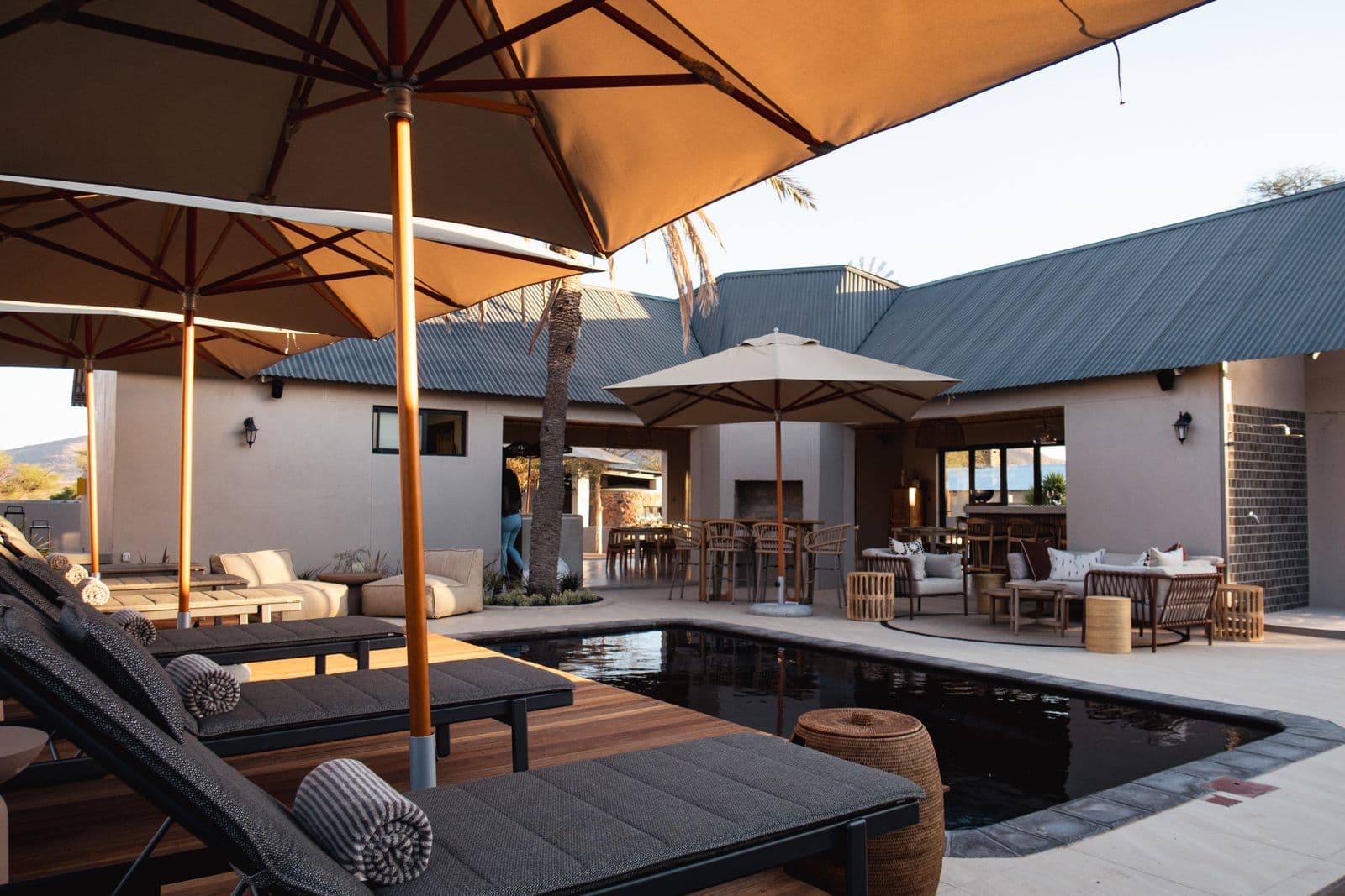 Der Pool mit Liegen unter Sonnenschirmen, dahinter die Lapa und die Poolside-Zimmer im Abendlicht.