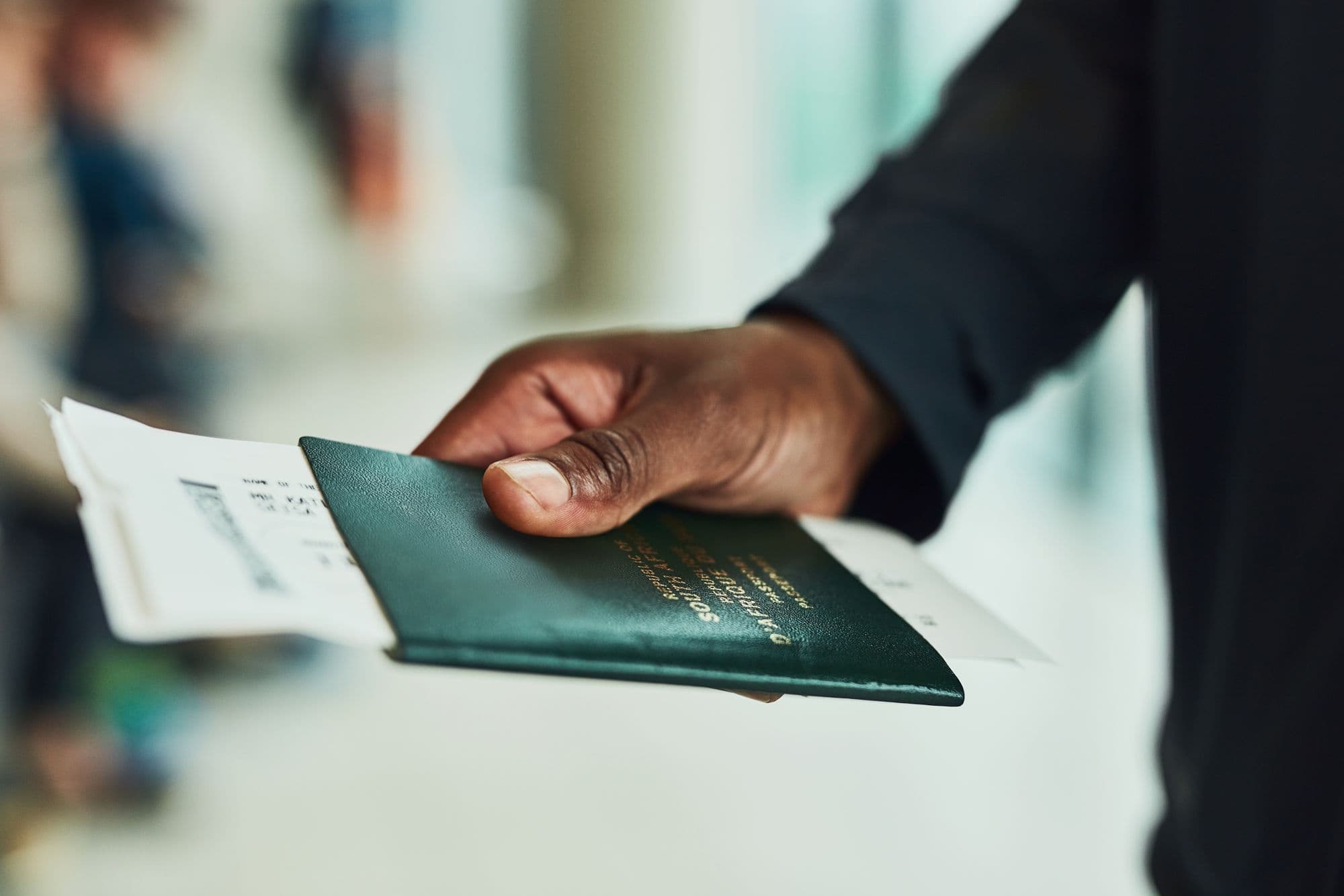 Eine Hand reicht einen grünen Reisepass mit Flugticket weiter.